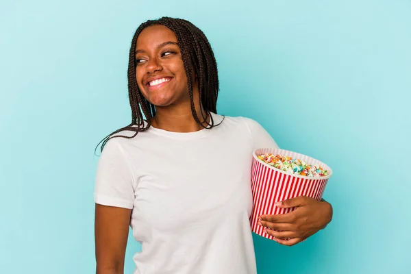 年轻的非洲裔美国女人吃着蓝色背景的爆米花 看上去面带微笑 快乐而愉快 — 图库照片