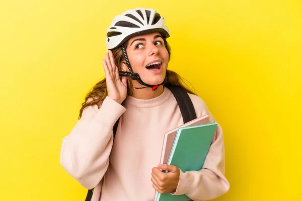 若いですCaucasian学生女性身に着けていますAバイクヘルメット隔離された上に黄色の背景に聞こうとしているゴシップ — ストック写真