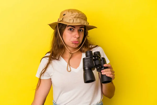 Young Caucasian Woman Holding Binoculars Isolated Yellow Background Shrugs Shoulders — Stock Photo, Image
