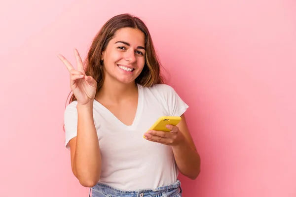Молодая Белая Женщина Мобильным Телефоном Розовом Фоне Показывает Номер Два — стоковое фото