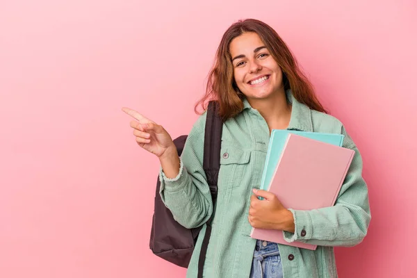 若い白人学生の女性はピンクの背景に描かれた本を笑顔で持ち 脇を指差して 空白のスペースで何かを示す — ストック写真