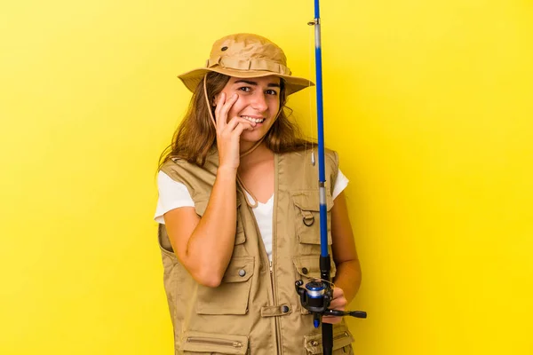 年轻的高加索女渔夫拿着一根用黄色背景隔离的钓竿 咬着指甲 紧张而焦虑 — 图库照片