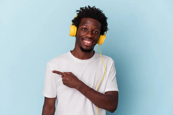 Joven Afroamericano Escuchando Música Aislada Sobre Fondo Azul Sonriendo Señalando —  Fotos de Stock