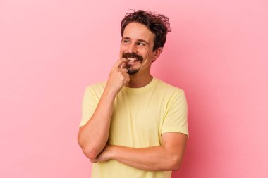 Pembe arka planda izole edilmiş genç beyaz adam rahatlamış bir şeyin fotokopi odasına baktığını düşünüyor..