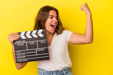 Elinde klaket tutan beyaz bir kadın sarı arka planda izole edilmiş zafer kazandıktan sonra yumruğunu kaldırıyor..