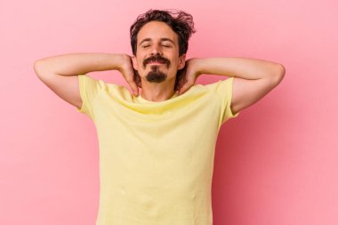 Pembe arka planda izole edilmiş genç beyaz bir adam kendini güvende hissediyor, elleri başının arkasında..