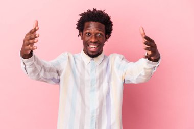 Genç Afrikalı Amerikalı bir adam pembe arka planda izole edilmiş zaferi ya da başarıyı kutluyor, şaşırmış ve şok olmuş..