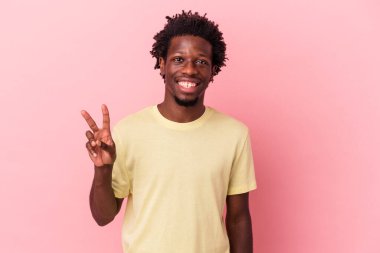 Genç Afrikalı Amerikalı adam pembe arka planda izole edilmiş zafer işareti gösteriyor ve geniş bir gülümseme sergiliyor..