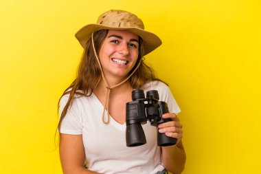Sarı arka planda dürbün tutan beyaz kadın gülüyor ve eğleniyor..