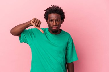Pembe arka planda izole edilmiş genç Afro-Amerikalı adam baş parmağını aşağı gösteriyor ve hoşlanmadığını ifade ediyor..