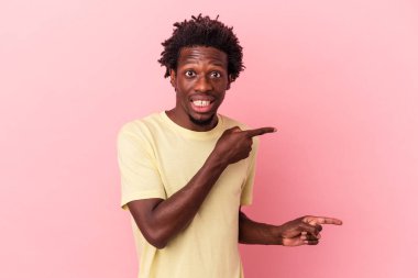 Pembe arka planda izole edilmiş genç Afrikalı Amerikalı adam işaret parmağıyla fotokopi alanını işaret ederek şok oldu..