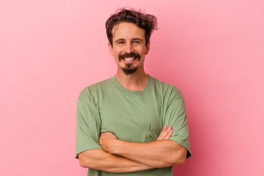 Pembe arka planda izole edilmiş genç beyaz adam kendini güvende hissediyor, kararlılıkla kollarını kavuşturuyor..