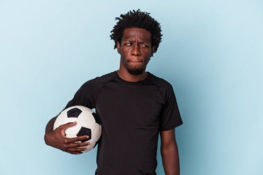 Amerikan futbolu oynayan genç Afro-Amerikalı adam mavi arka planda izole edilmiş, kafası karışmış ve kendinden emin değil..