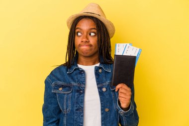 Sarı arka planda izole edilmiş pasaportu olan genç Afrikalı Amerikalı kadın kafası karışmış ve kendinden emin değil..