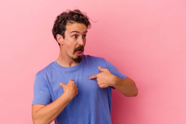 Pembe arka planda izole edilmiş genç beyaz adam parmağını göstererek şaşırdı, geniş bir gülümsemeyle..