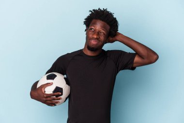Amerikan futbolu oynayan genç Afro-Amerikalı adam mavi arka planda izole edilmiş kafasının arkasına dokunuyor, düşünüyor ve bir seçim yapıyor..