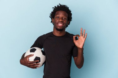 Amerikan futbolu oynayan genç Afro-Amerikalı adam mavi arka planda izole edilmiş neşeli ve kendinden emin..
