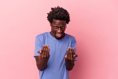 Pembe arka planda izole edilmiş genç Afro-Amerikan erkeği sanki seni davet ediyormuş gibi parmağıyla işaret ediyor..