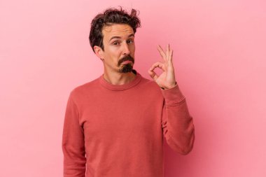 Pembe arka planda izole edilmiş genç beyaz bir adam bir göz kırptı ve elleriyle iyi bir jest yaptı..