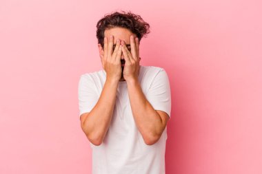 Pembe arka planda izole edilmiş genç beyaz adam kameraya parmaklarıyla göz kırpıyor, yüzünü kapatmaktan utanıyor..