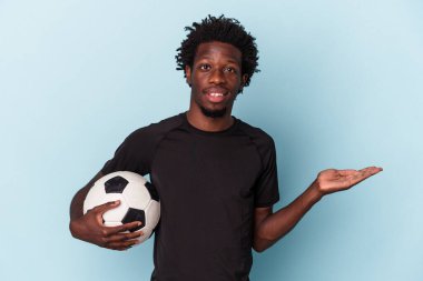 Amerikan futbolu oynayan genç Afrikalı bir adam mavi arka planda izole edilmiş bir şekilde bir avuç içinde fotokopi alanı ve belinde başka bir el tutuyor..