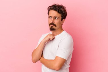 Pembe arka planda soyutlanmış, kafası karışmış, şüpheli ve kararsız genç bir beyaz adam..