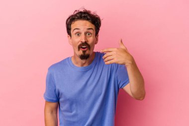 Pembe arka planda izole edilmiş genç beyaz bir adam bir şeye gülüyor, elleriyle ağzını kapatıyor..