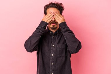 Pembe arka planda izole edilmiş genç beyaz adam elleriyle gözlerini kapatmaktan korkuyor..