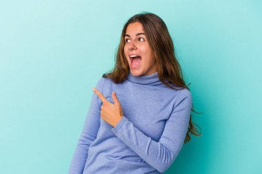 Mavi arka planda soyutlanmış genç beyaz kadın gülümseyen, neşeli ve keyifli bir tarafa bakıyor..