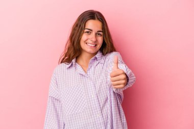 Pembe arka planda izole edilmiş genç beyaz kadın gülümsüyor ve başparmağını kaldırıyor.