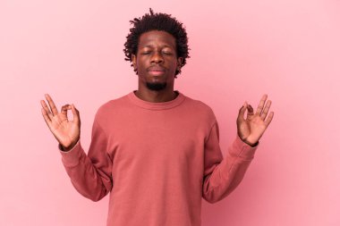 Genç Afrikalı Amerikalı adam pembe arka planda izole edilmiş yoğun bir günün ardından dinleniyor. Yoga yapıyor..