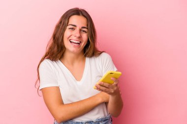 Pembe arka planda izole edilmiş cep telefonu kullanan beyaz bir kadın gülüyor ve eğleniyor..