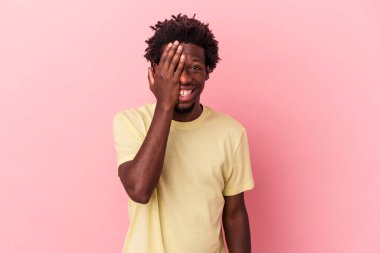 Genç Afrikalı Amerikalı bir adam pembe arka planda izole edilmiş. Yüzünün yarısını palmiye ile örterek eğleniyor..