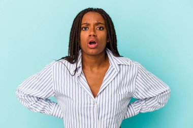 Genç Afrikalı Amerikalı bir kadın mavi arka planda izole edilmiş. Gördüğü bir şey yüzünden şoka uğruyor..