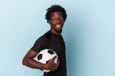 Mavi arka planda izole bir şekilde futbol oynayan Afrikalı genç bir Amerikalı gülümsüyor ve keyifli görünüyor..