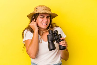 Dürbün tutan genç beyaz kadın sarı arka planda izole edilmiş kulakları elleriyle kapatıyor..