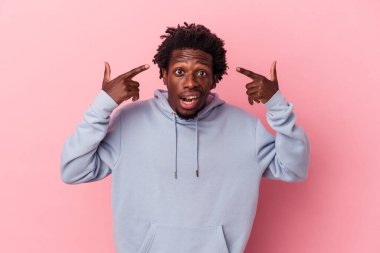 Pembe arka planda izole edilmiş genç Afro-Amerikalı adam işaret parmağıyla hayal kırıklığı jesti yapıyor..
