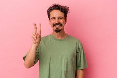 Genç beyaz adam pembe arka planda izole edilmiş neşeli ve kaygısız parmakları olan bir barış sembolü gösteriyor..