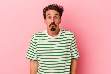 Pembe arka planda izole edilmiş genç beyaz adam omuzlarını silkeliyor ve gözleri açık..