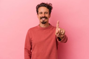 Pembe arka planda izole edilmiş genç beyaz bir adam bir numarayı parmağıyla gösteriyor..