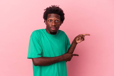 Pembe arka planda izole edilmiş genç Afrikalı Amerikalı adam işaret parmağıyla fotokopi alanını işaret ederek şok oldu..