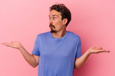 Kafkasyalı genç adam pembe arka planda izole edilmiş. Kafası karışmış ve omuz silkiyor. Kopya alanını tutmak için..