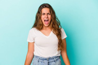 Kafkasyalı genç bir kadın mavi arka planda izole edilmiş çok kızgın, öfkeli, hayal kırıklığına uğramış bağırıyor..