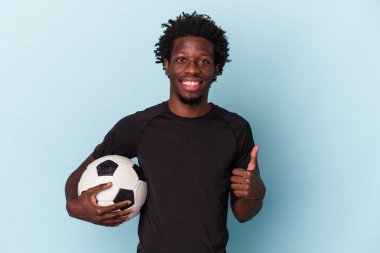 Amerikan futbolu oynayan genç Afrikalı adam mavi arka planda izole edilmiş gülümsüyor ve başparmağını kaldırıyor.