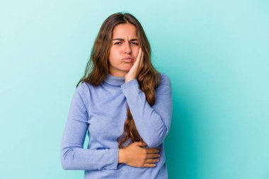 Mavi arka planda izole edilmiş genç beyaz kadın yanakları patlatıyor, yorgun bir ifadesi var. Yüz ifadesi kavramı.