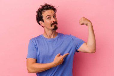 Pembe arka planda izole edilmiş genç beyaz bir adam güçlü bir hareket gösteriyor, kollarıyla, kadınsı gücün sembolü.