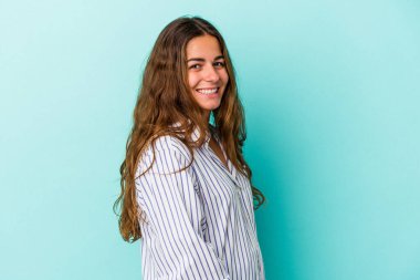 Kafkasyalı genç bir kadın mavi arka planda izole edilmiş. Kendine güvenen, ellerini kalçasında tutan..