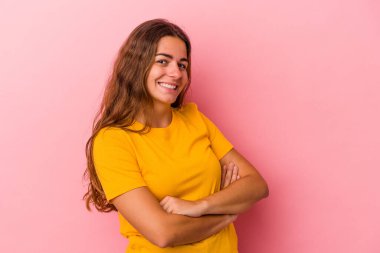 Pembe arka planda soyutlanmış genç beyaz kadın kendini güvende hissediyor, kararlılıkla kollarını kavuşturuyor..