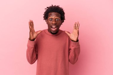 Genç Afrikalı Amerikalı bir adam pembe arka planda izole edilmiş zaferi ya da başarıyı kutluyor, şaşırmış ve şok olmuş..