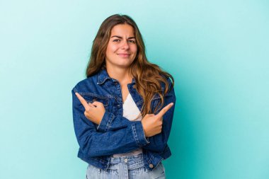 Mavi arka plan noktalarında izole edilmiş genç beyaz kadın iki seçenek arasında seçim yapmaya çalışıyor..